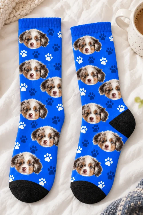 Pair of royal blue paw print socks with puppy faces laid flat beside a coffee cup