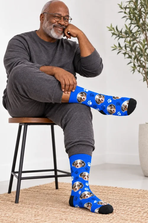 Older man in glasses on a stool showing royal blue paw face socks for men