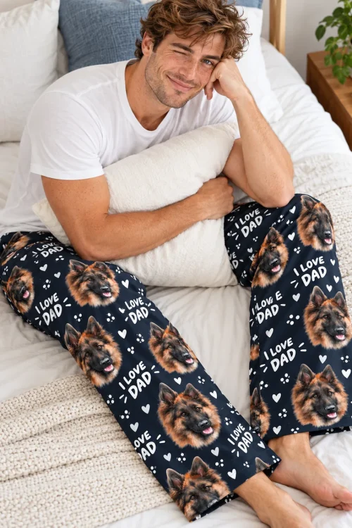 Man hugging a pillow on a bed in navy Father's Day pajama pants printed with German Shepherd faces