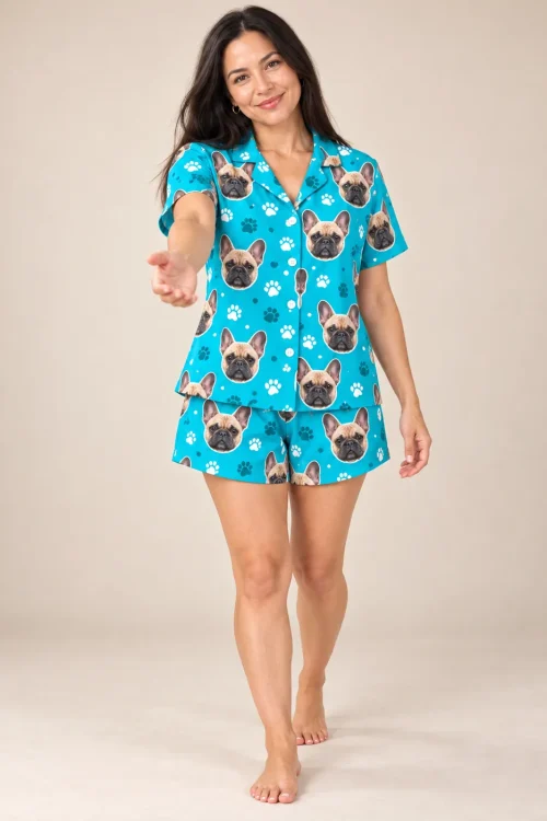 Smiling woman reaching toward the camera in a teal paws frenchie pj set, barefoot in a beige studio