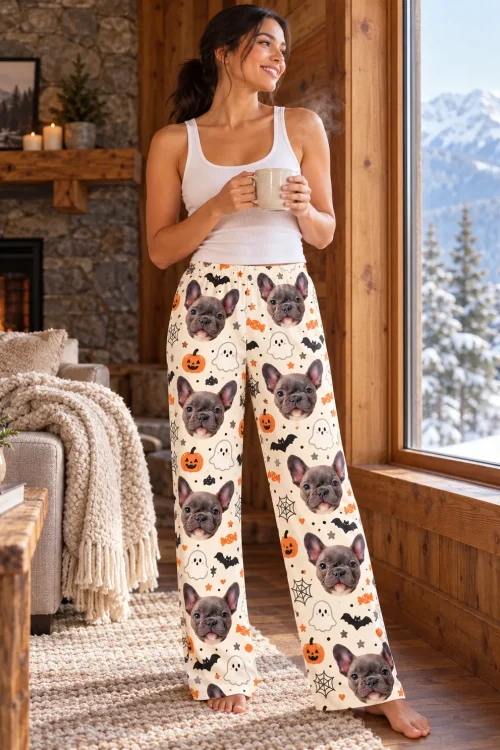 Woman with a mug by a mountain-view window in Halloween pajama pants with French bulldog faces