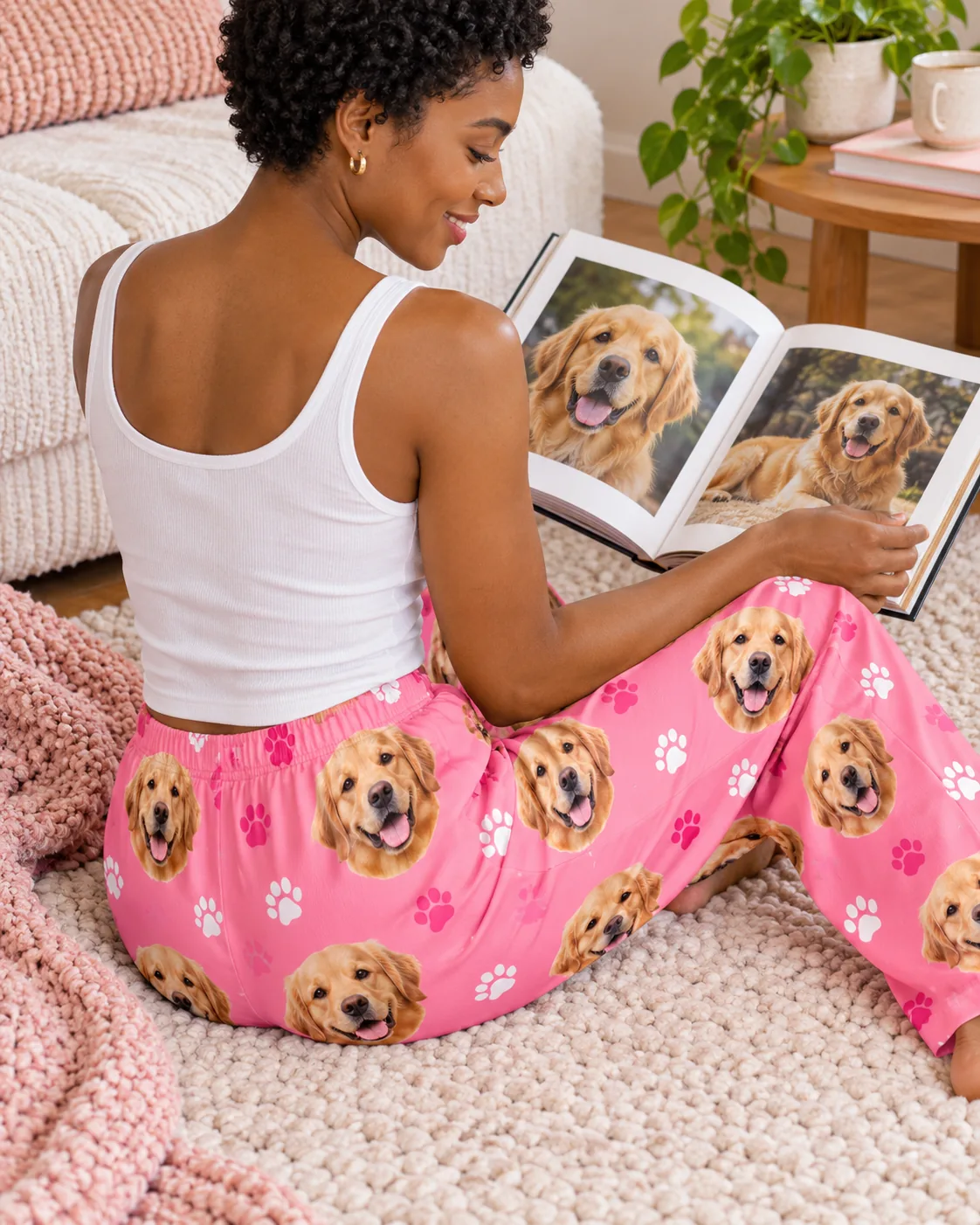 Woman on a rug looking at a golden photo book in pink paws golden retriever pajama pants, back view