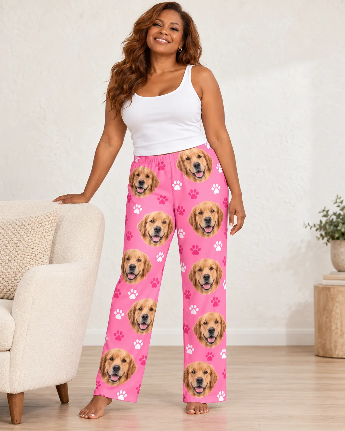 Smiling woman in a white tank and pink paws golden retriever pajamas for women, hand on a cream armchair