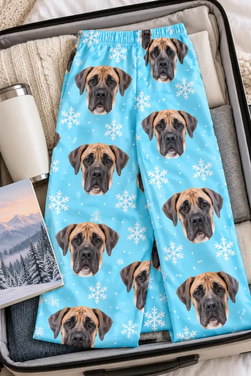 Snowflake great dane pajama pants laid flat in an open suitcase with a travel mug and a notebook