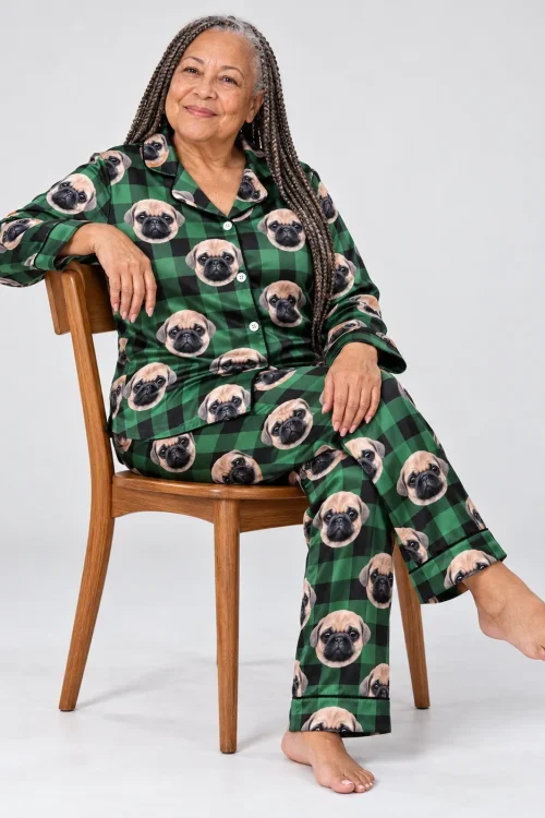 Woman with long braids seated on a wooden chair in a green plaid pajama set with pug faces