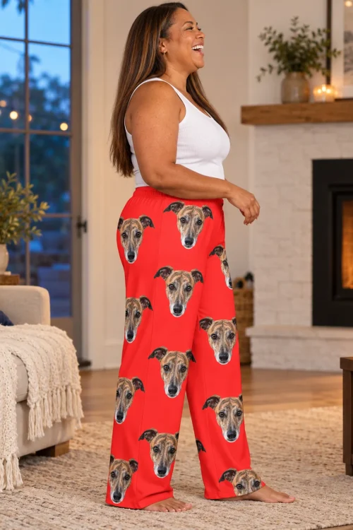 Woman laughing by a lit fireplace, side view of red greyhound pajamas with dog faces down the leg