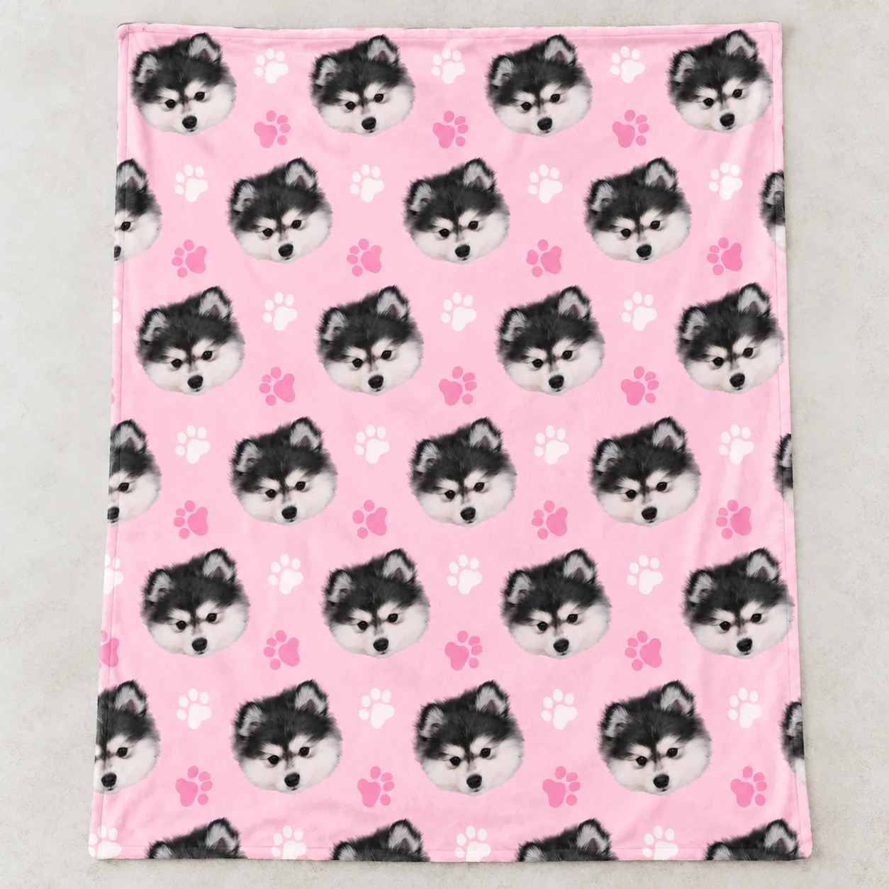Pink pet blanket laid flat, printed with a husky's face and paw prints