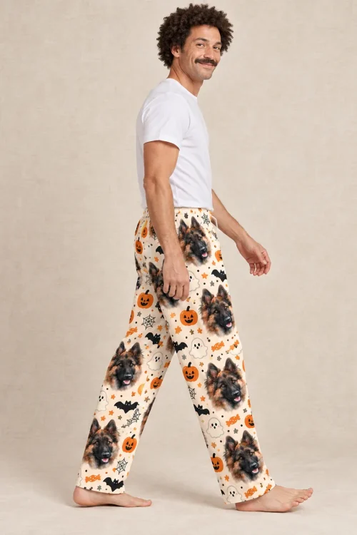 Man walking in cream Halloween pajama pants with German Shepherd faces and pumpkins on a beige backdrop