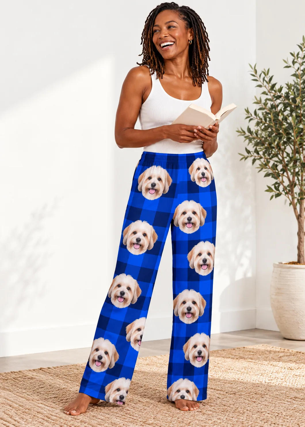 Woman reading a book in blue plaid havanese pajamas with cream dog faces on both legs, bright white room