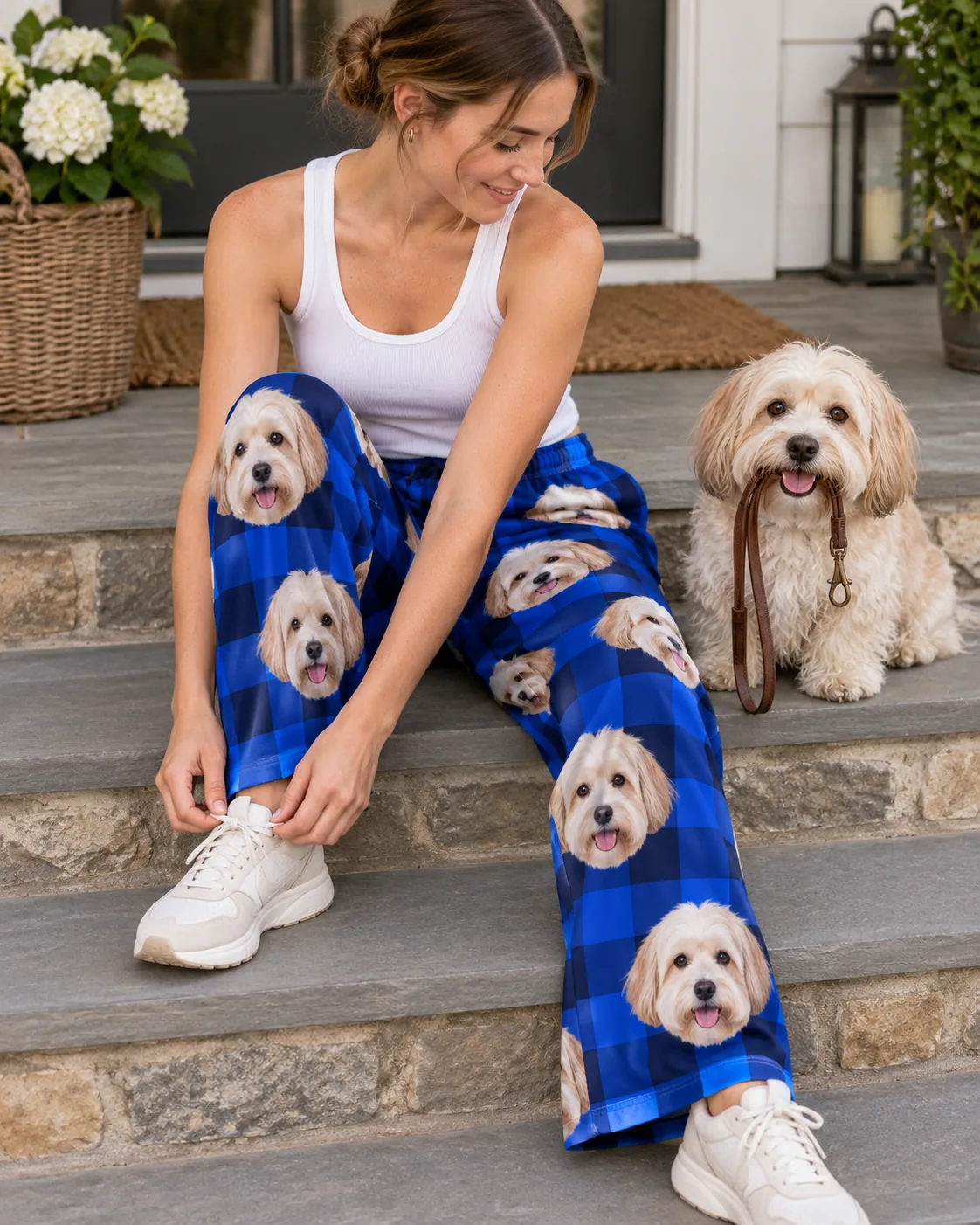 Woman tying her sneaker on stone steps in blue plaid havanese pajamas, her cream Havanese holding a leash
