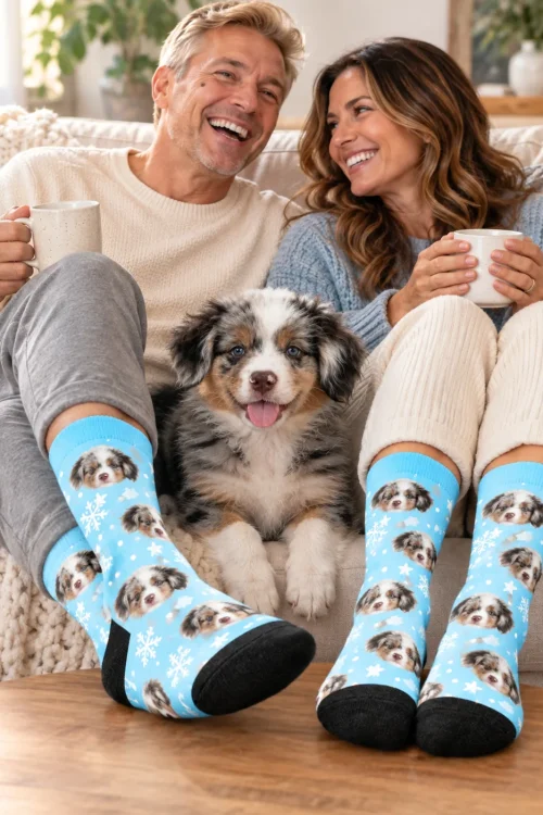 Couple with mugs on a sofa in snowflake face socks, their puppy between them