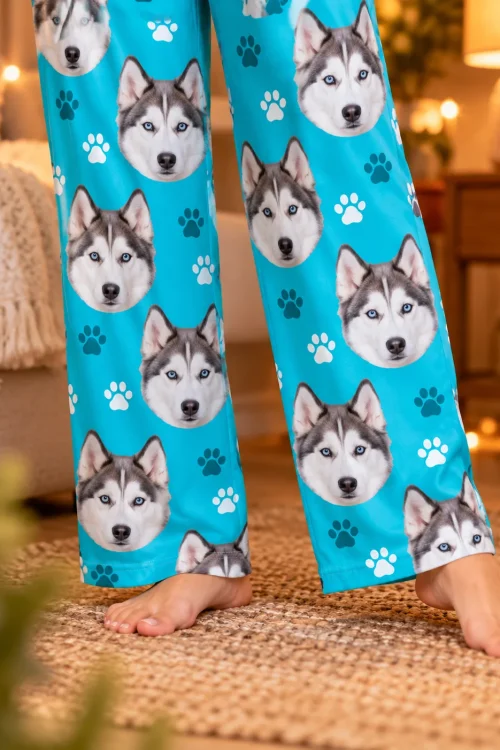 Close view of teal paws husky dog pajama pants with blue-eyed husky faces, bare feet on a woven rug