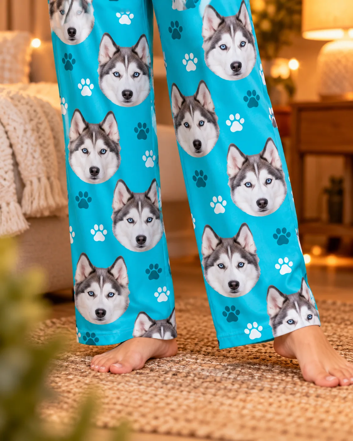 Close view of teal paws husky dog pajama pants with blue-eyed husky faces, bare feet on a woven rug