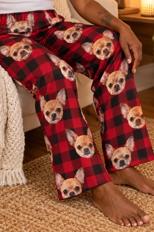 Close-up of a seated woman's legs in red plaid pajama pants covered in chihuahua faces, on a jute rug