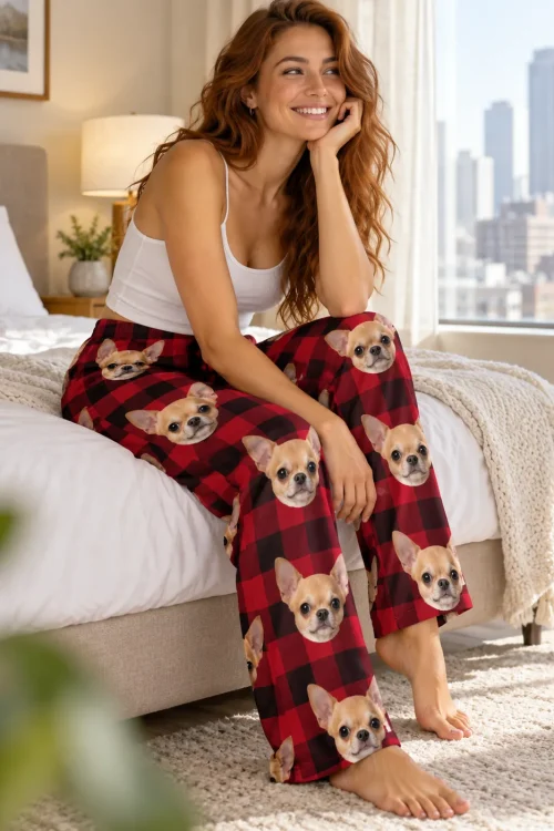 Woman sitting on the edge of a bed by a city window in red plaid chihuahua pajama pants