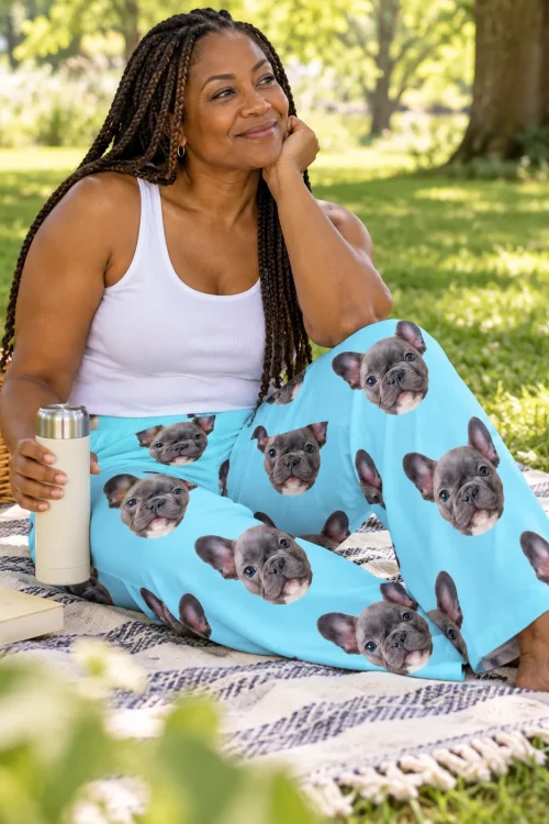 Woman with braids on a park picnic blanket in light blue pajama pants printed with French bulldog faces