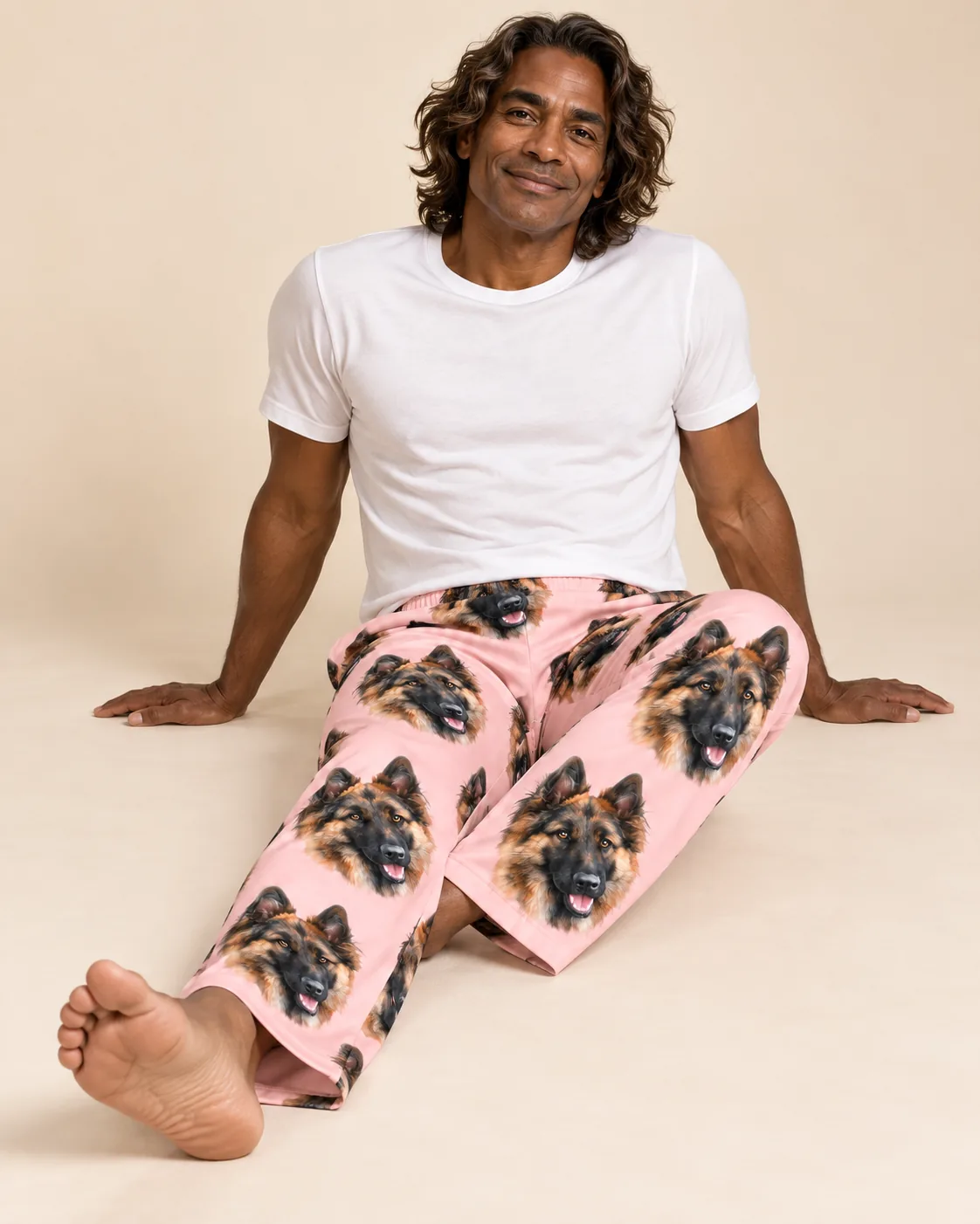 Man sitting on a studio floor in light pink pajama pants printed with German Shepherd faces