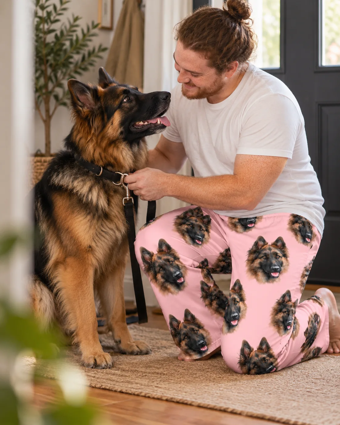 Man clipping a leash on his German Shepherd while kneeling in light pink pet face pajama pants