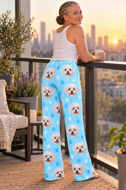 Woman seen from behind on a city balcony at sunset, holding a mug, in light blue paws maltese face pajama pants