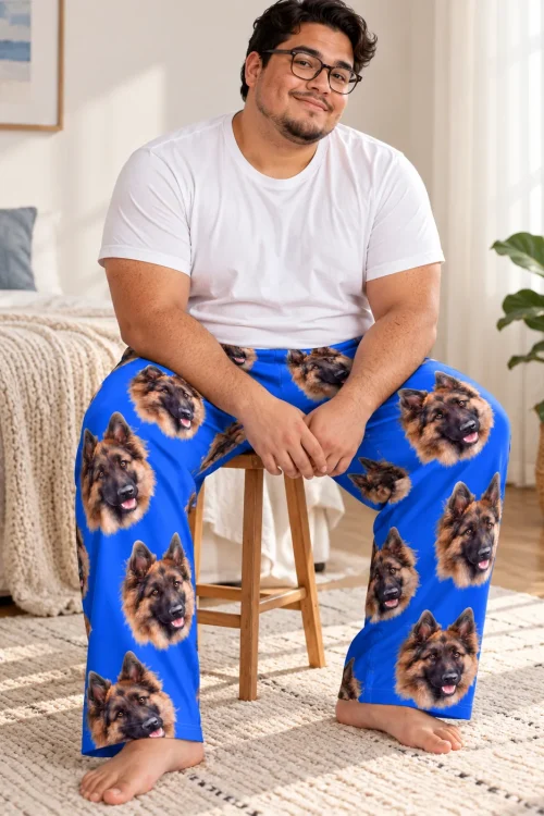 Man seated on a wooden stool in blue pajama pants covered in German Shepherd faces