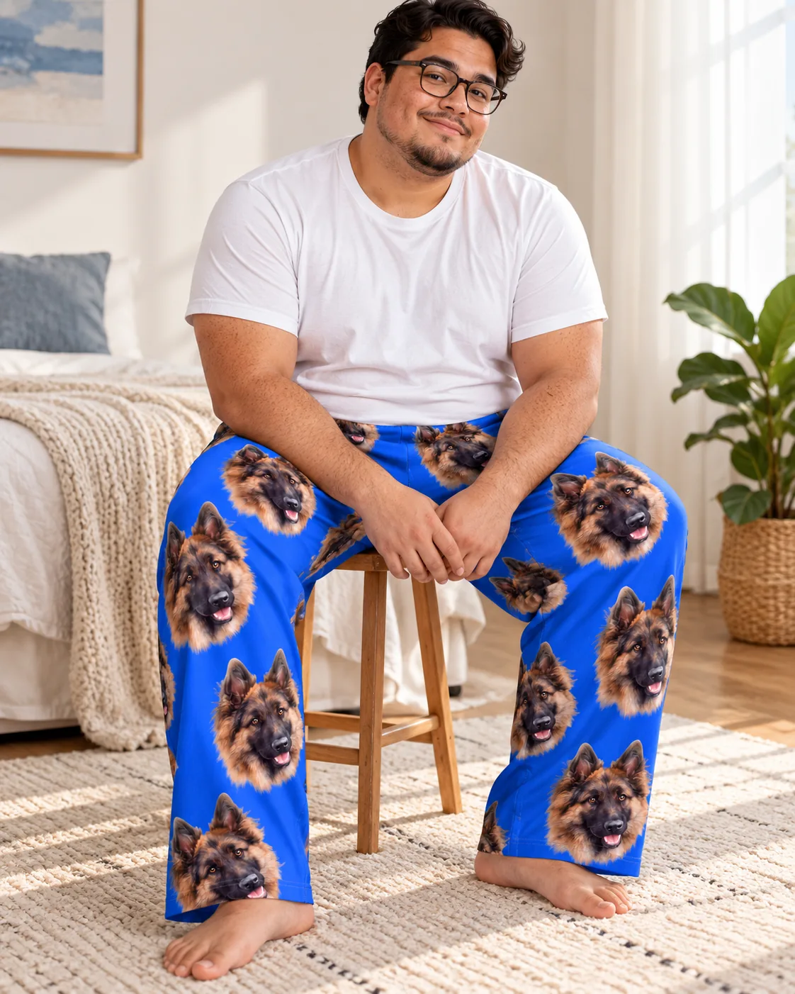 Man seated on a wooden stool in blue pajama pants covered in German Shepherd faces