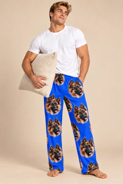Man holding a cream pillow in royal blue pajama pants with German Shepherd faces on a beige backdrop