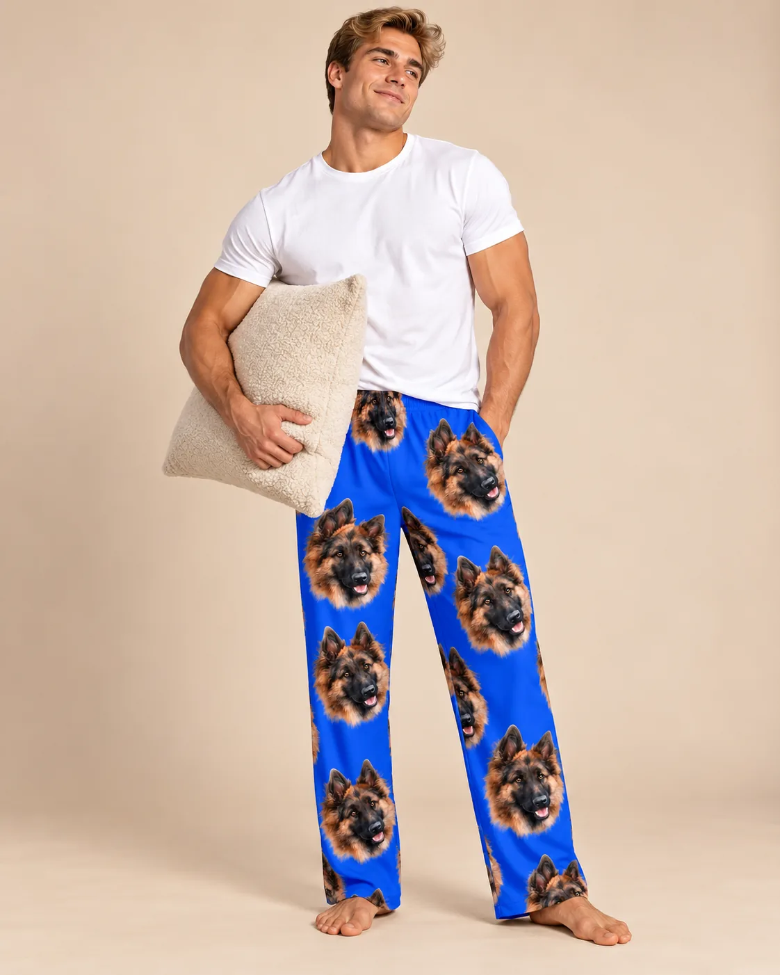 Man holding a cream pillow in royal blue pajama pants with German Shepherd faces on a beige backdrop