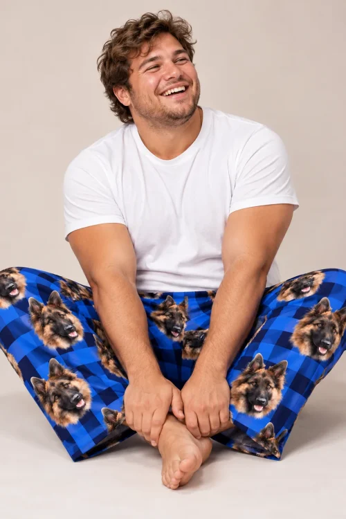 Laughing man sitting cross-legged in blue plaid pajama pants printed with German Shepherd faces