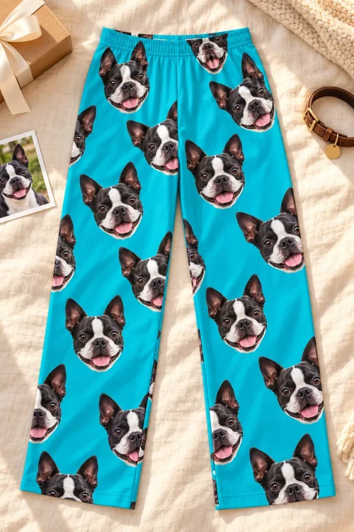 Teal Boston terrier pajama pants laid flat on a cream blanket beside a gift box, a dog collar and a printed dog photo