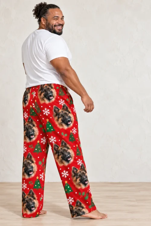 Man in a white tee wearing red mens Christmas pajama pants with German Shepherd faces, trees and snowflakes