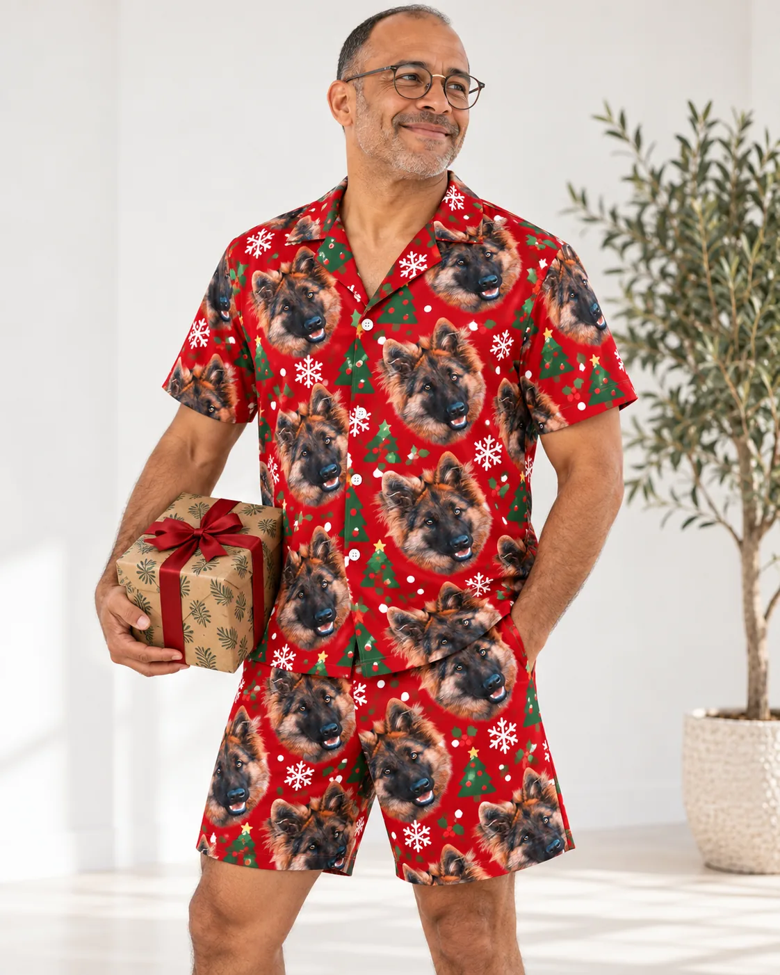 Man holding a wrapped gift in a red Christmas pajama set with German shepherd faces, trees and snowflakes