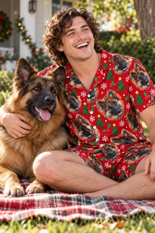 Man on a plaid blanket on the lawn hugging his German shepherd, wearing a Christmas pajama set with its face