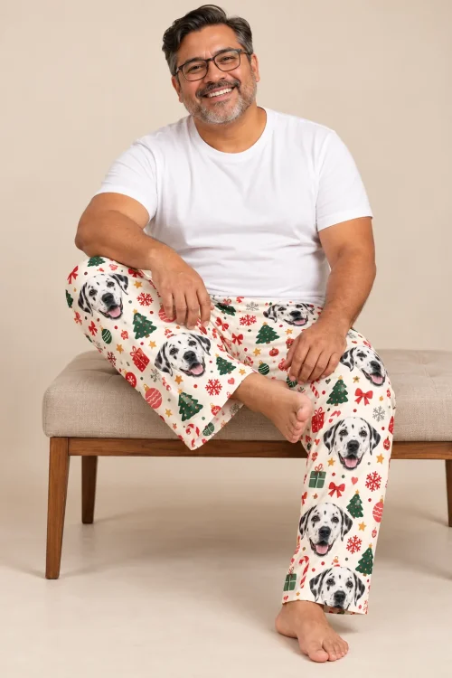 Man in glasses on an upholstered bench in Christmas cream dalmatian pajama pants, beige backdrop