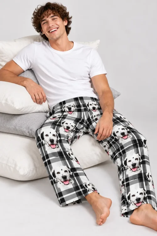 Curly-haired man leaning on stacked pillows in white plaid mens dalmatian pajamas, light gray studio