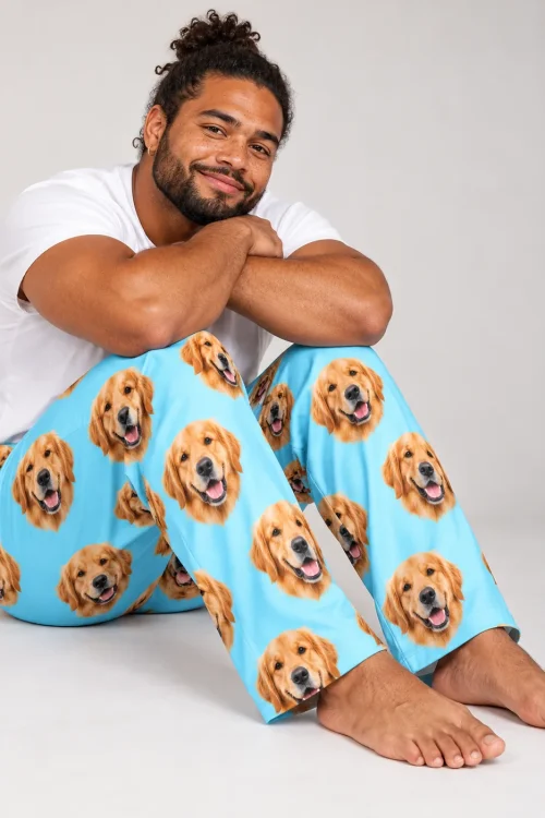 Smiling man sitting on a studio floor in light blue golden retriever pajama pants, arms on his knees