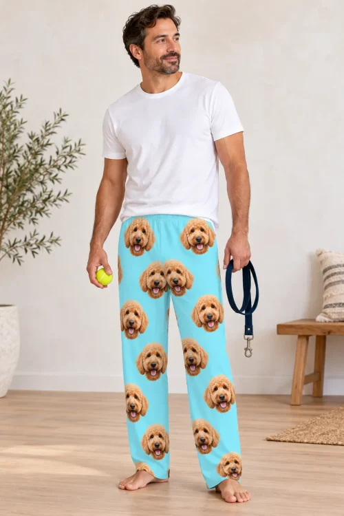 Man holding a tennis ball and a navy leash in light blue goldendoodle pajama pants covered in doodle faces