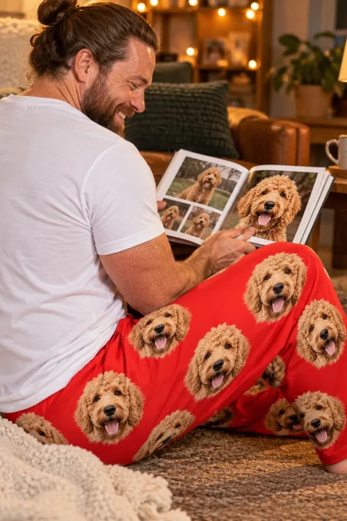 Man on the rug paging through a goldendoodle photo book in red pajama pants printed with doodle faces