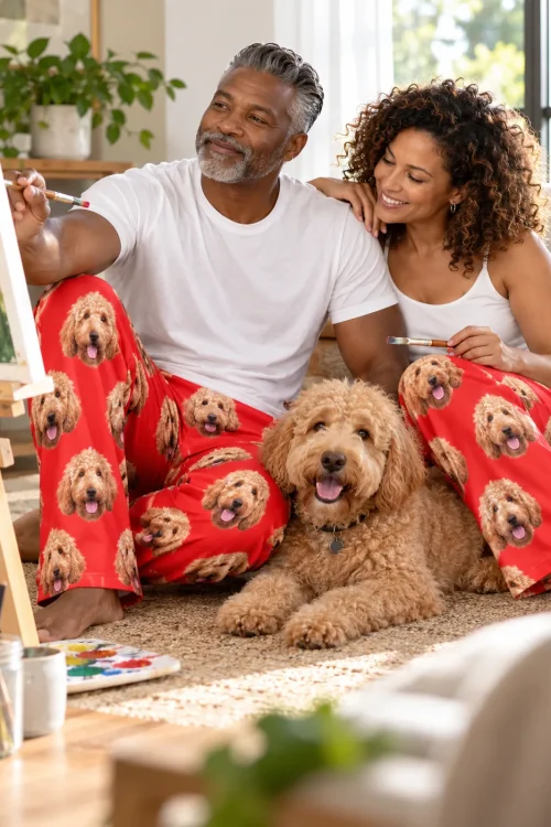Couple painting on a sunny rug in red goldendoodle pajama pants, their curly doodle lying between them