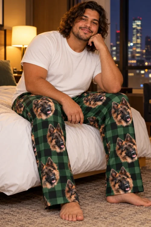 Man on a hotel bed with a city view at night in green plaid pajama pants with German Shepherd faces