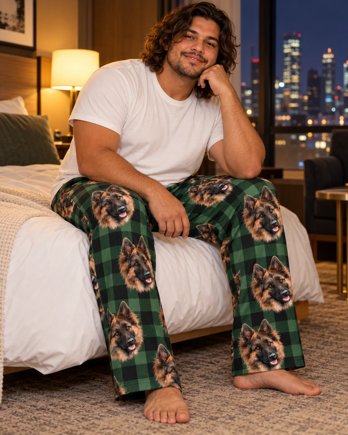 Man on a hotel bed with a city view at night in green plaid pajama pants with German Shepherd faces