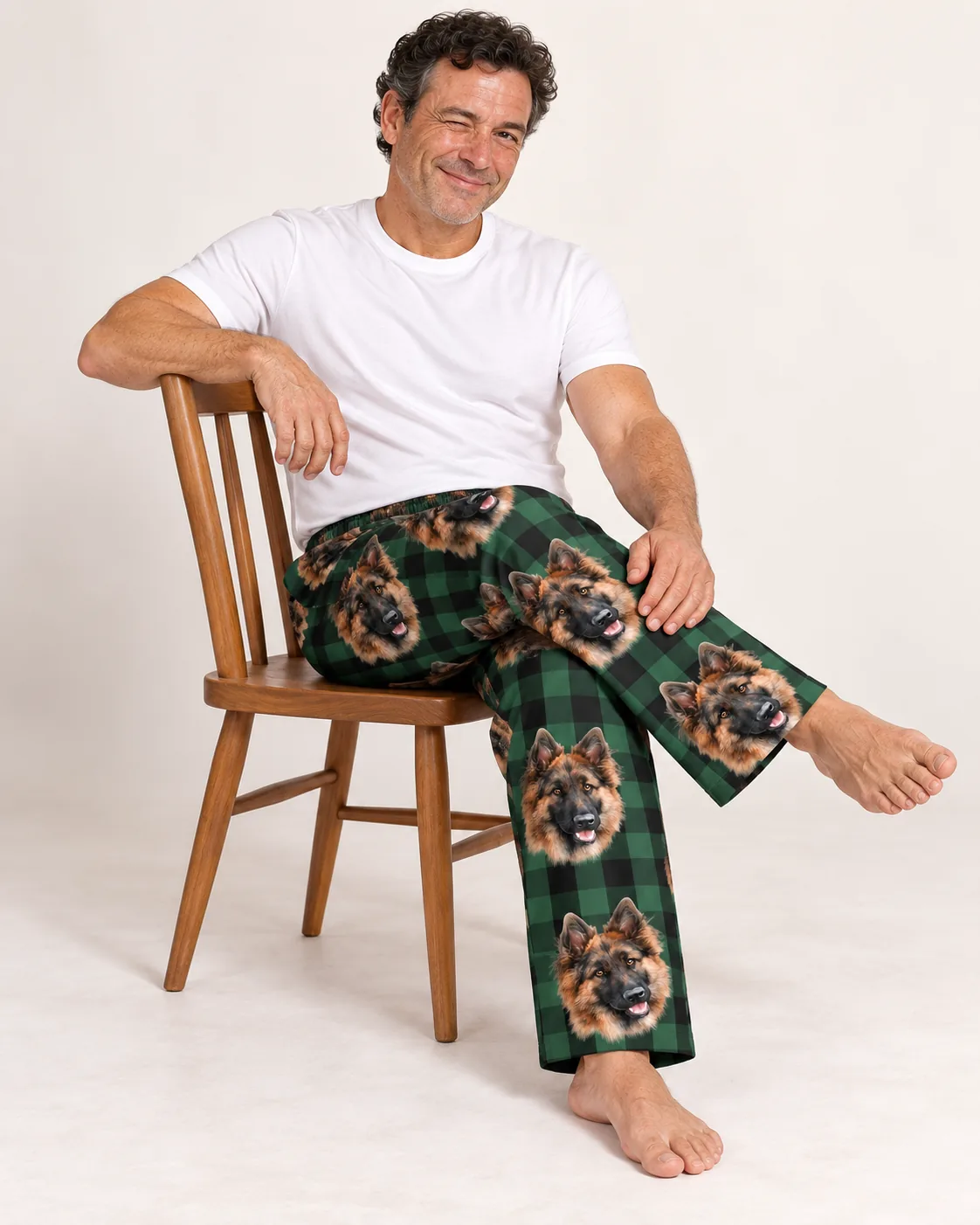 Man winking on a wooden chair in green plaid pajama pants with German Shepherd faces