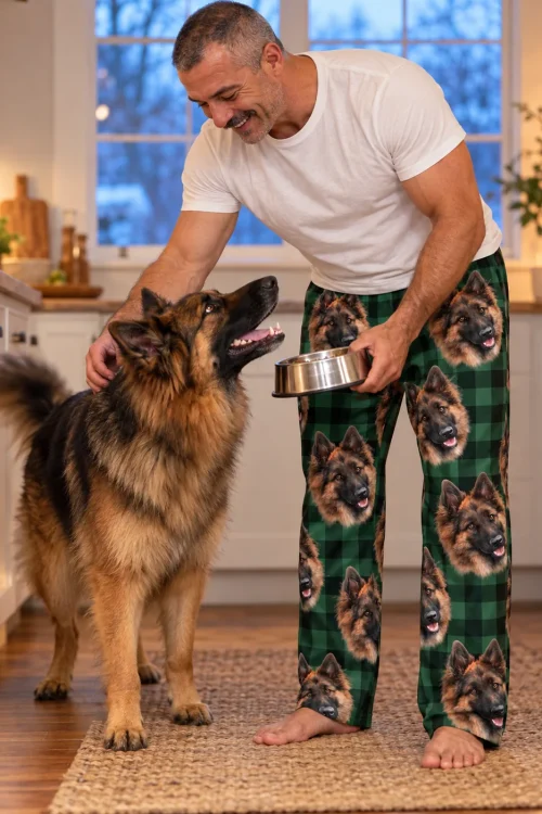 Man feeding his German Shepherd in the kitchen, wearing green plaid pajama pants with its face