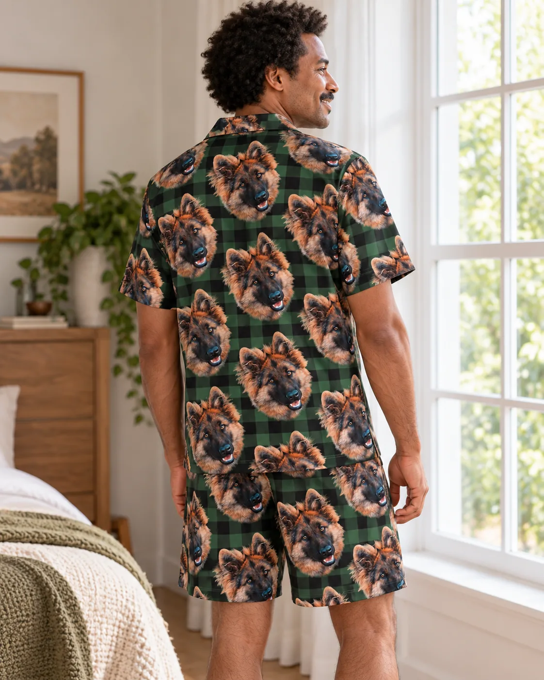 Back view of a man in green and black plaid pajamas with German shepherd faces by a bright window