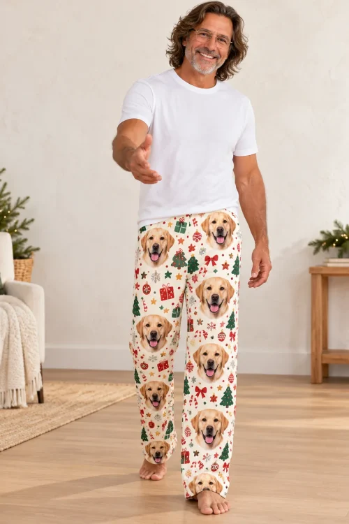 Smiling man in glasses reaching out a hand in Christmas cream labrador pajama pants by a small tree