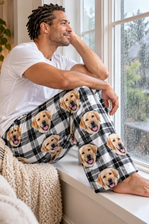 Man on a window seat watching the rain in white plaid pajama pants printed with labrador faces