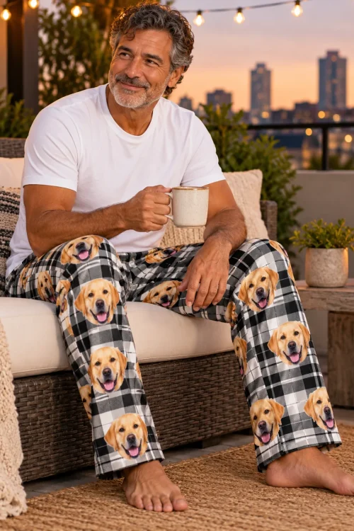 Man with a mug on a rooftop sofa at dusk in white plaid labrador pajama pants, city lights behind