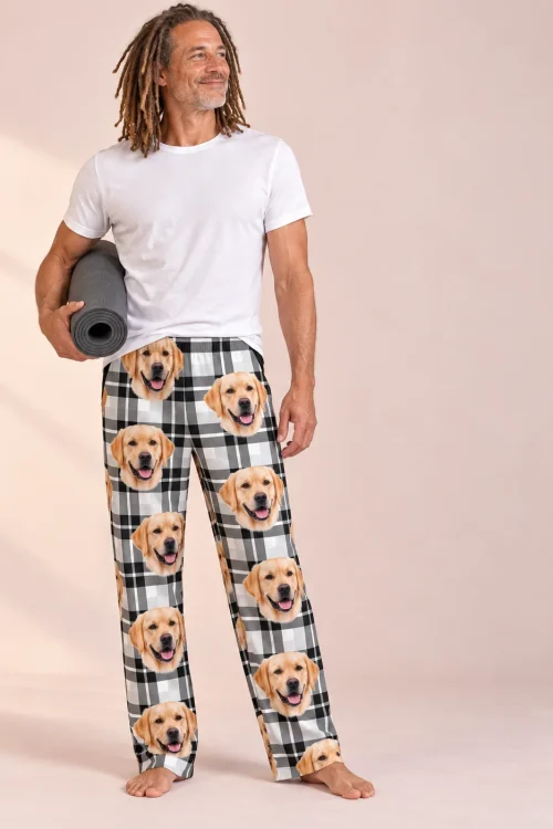 Man with gray locs holding a yoga mat in white plaid labrador pajama pants, soft pink studio