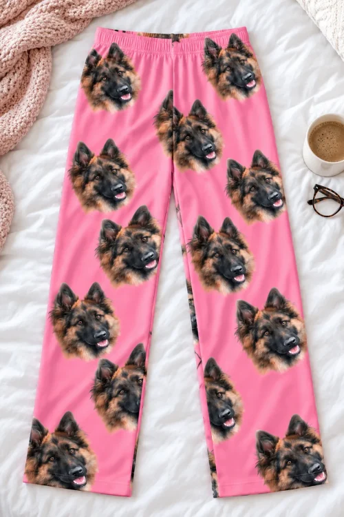Pink pajama pants with German Shepherd faces laid flat on a white bed beside coffee and glasses