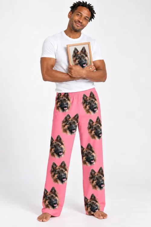 Smiling man in a white tee and pink pajama pants with German Shepherd faces, hugging a framed dog photo