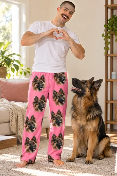 Man making a heart with his hands beside his German Shepherd, in pink pajama pants printed with its face